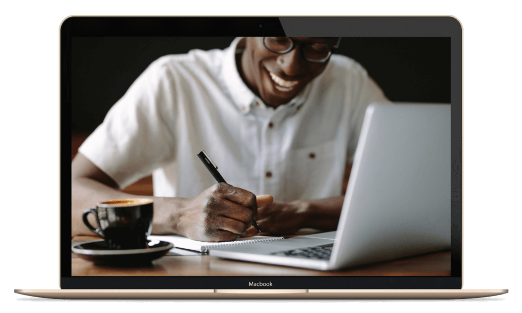 A Black Man Sits at His Laptop Smiling While Taking Notes