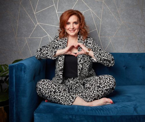 Tricia Brouk Dressed in a Leopard Print Suit Holding Her Hands in a Heart Shape